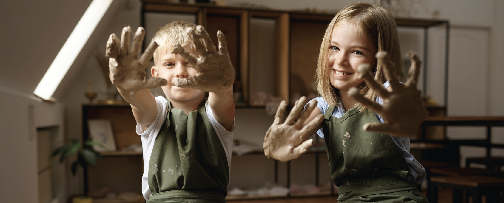 Kinder zeigen ihre mit Ton bedeckten Hände beim kreativen Töpfern